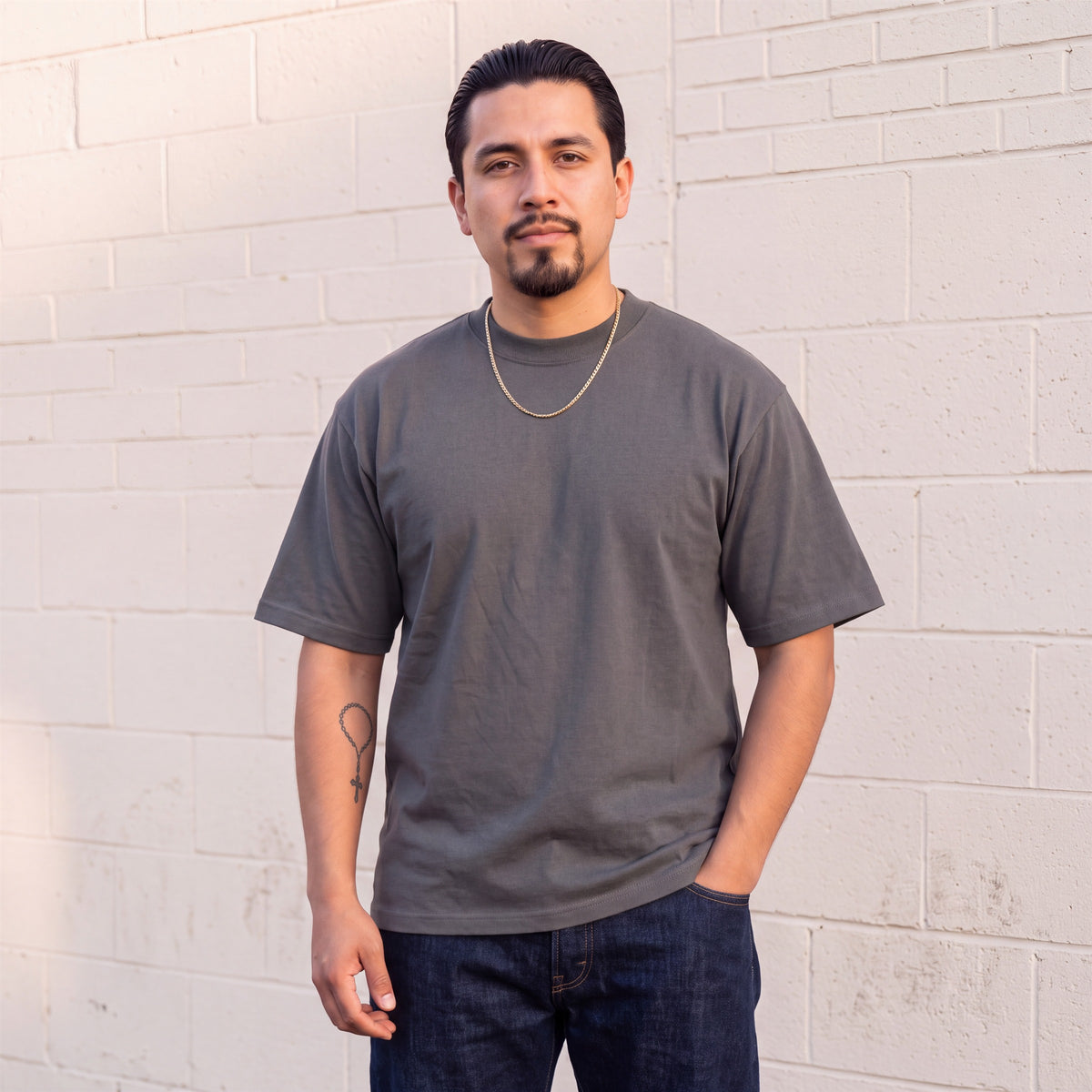 Model wearing Shaka Wear 7.5 oz Max Heavyweight Short Sleeve T-Shirt in Dark Grey